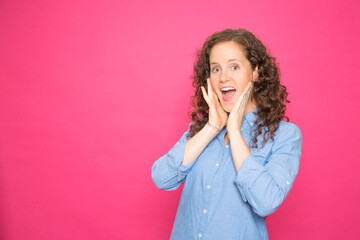 Portrait surprised young girl with hands on face looking at camera over pink background