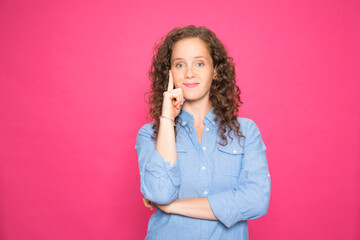 Portrait happy young girl with pensive pose looking at camera wearing blue shirt on pink background