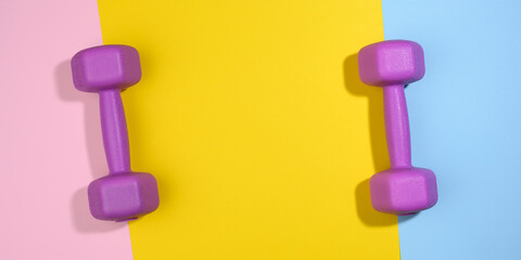 two purple plastic kilogram dumbbells on a bright colored background, top view.