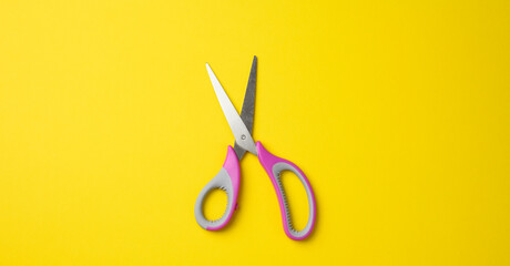 metal scissors with pink plastic handle on a yellow background
