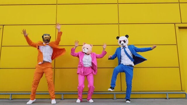 Business people wearing animal masks jumping in front of yellow wall