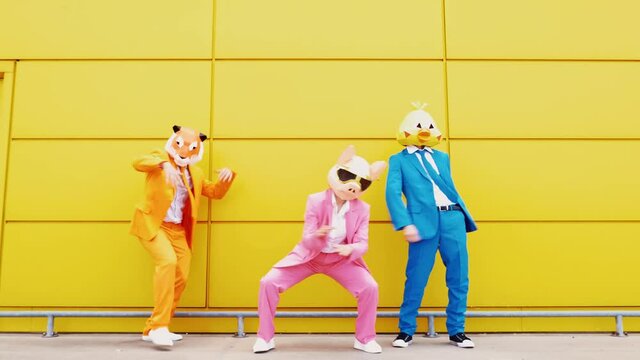 Business people wearing animal masks dancing in front of yellow wall