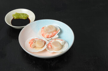 Natural raw scallop with boiled shrimp in the sink in a ceramic bowl with soy sauce and wasabi on a dark background.