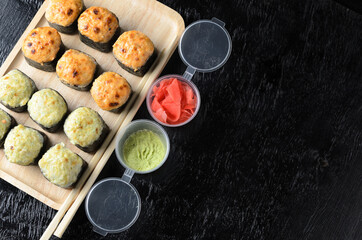 A set of seafood rice rolls wrapped in thin dried sea grass leaves on a wooden platter with ginger and wasabi