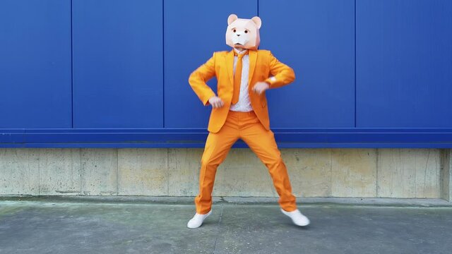 Man with bear mask running and dancing in front of blue wall