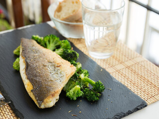 fried fillet of sea bass with garnish of broccoli on black warm stone plate