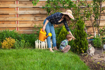 Child and mother watering can watering a garden in the backyard