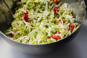 Salad of green Chinese cabbage, peppers and herbs in a silver bowl with spoons in it on a white background