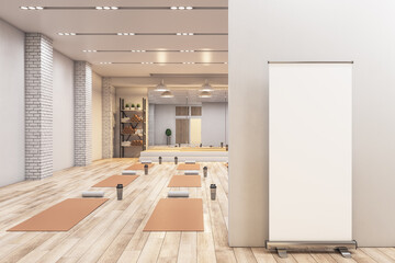 Modern concrete yoga gym interior with equipment, blank frame on wall, daylight and wooden...