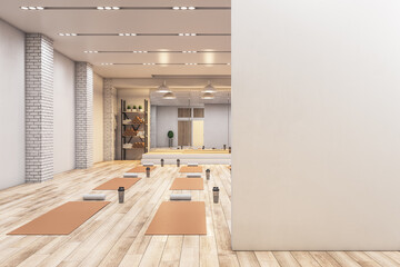 Bright concrete yoga gym interior with equipment, blank mockup space on wall, daylight and wooden...