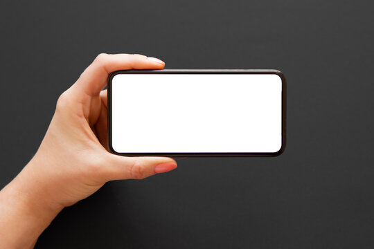 Person holding phone horizontally in one hand on dark background