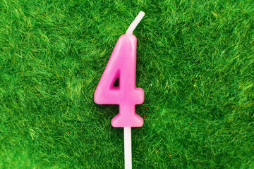 candle in the form of number 4 on the green grass background, a place for a greeting text