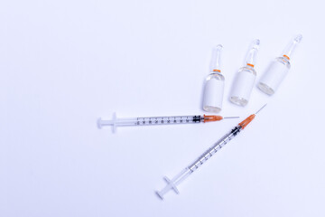 Two syringes placed on an isolated white background next to three glass vials with blank labels with room for text, top view.