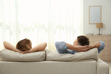 Couple relaxing on sofa in living room, back view