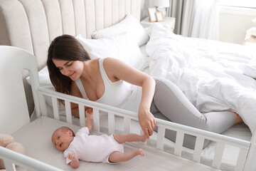 Obraz na płótnie Canvas Happy young mother near bedside crib with her cute newborn baby at home