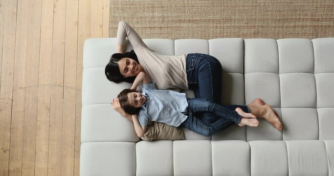 Serene mom and son enjoy day nap on cozy soft sofa, above view. Asian nanny and preschool boy take break breath conditioned air relaxing at home. Carefree leisure weekend time at modern flat concept - Powered by Adobe