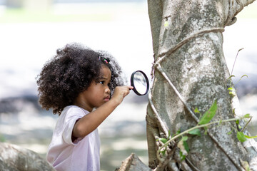 Close-up of a cute Afro-haired girl looking at a tree through a magnifying glass.