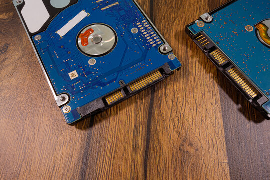 Close-up: two hard drives from a laptop lie on a surface with a wooden texture. Blue-green textolite and a SATA connector.