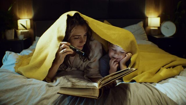 Young mother reading a book in the bed to son