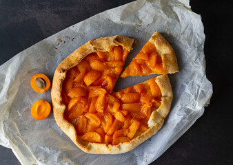 Delicious homemade French galette with ripe sweet apricots on a smooth dark background. Flat lay. Fresh handmade vegan food. Sweet pastries with apricots.
