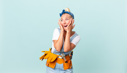 pretty blond woman feeling happy, excited and surprised and repairing house concept