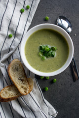 Green peas soup in a white bowl, fresh baguette bread on striped kitchen towel. Vegetarian meal top view photo. Eating fresh concept.  