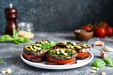 Eggplant and tomato appetizer with pesto sauce on a concrete kitchen table. Eggplant appetizer with nuts.