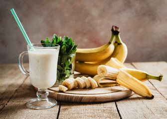 Delicious Banana Yogurt Smoothie in a latte coffee glass with handle with mint leaves and bananas with handle on wooden background