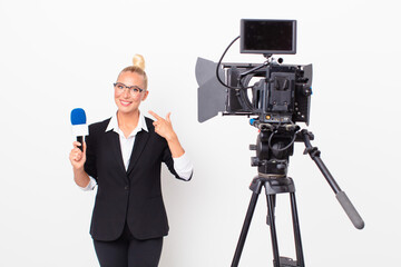 pretty blond woman smiling confidently pointing to own broad smile and holding a pmicrophone....