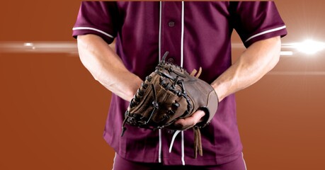 Mid section of male baseball pitcher wearing gloves against spot of light on orange background