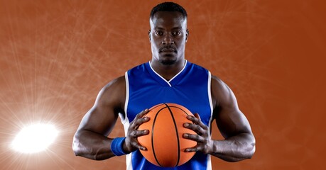 African american male basketball player holding basketball against spot of light in background