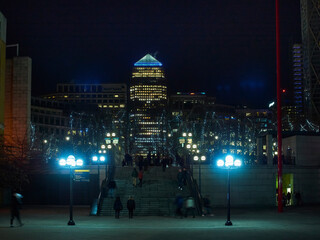 Looking up a staircase to the soaring, illuminated Canada Tower, with a crowd of motion-blurred...