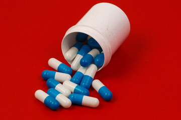heap of blue and white capsules are falling out of a white cup in the red studio