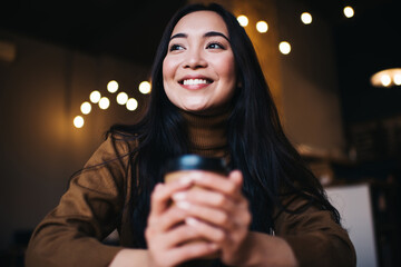 Happy Caucasian woman 20 years old holding takeaway cup with hot caffeine beverage and dreaming,...