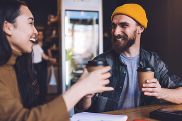 Prosperous male and female friends satisfied with sincerely conversation during coffee break from organisation planning in cafe interior, joyful hipster students holding takeaway cups and laughing