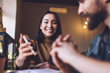Positive lady showing smartphone to boyfriend while sitting in cafe
