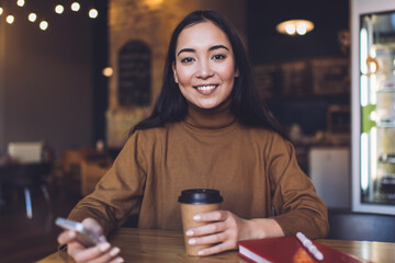 Happy young woman with smartphone in coffee shop
