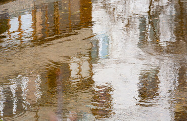Spring cloudy day. A large puddle reflects an apartment building with balconies.