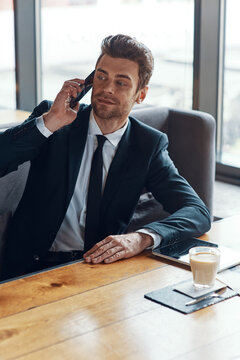 Handsome young businessman in full suit talking on the smart phone while sitting in the restaurant