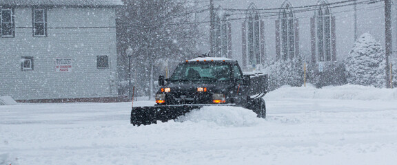Black truck with a snowplow clearing a parking lot behind buisnesses © coachwood
