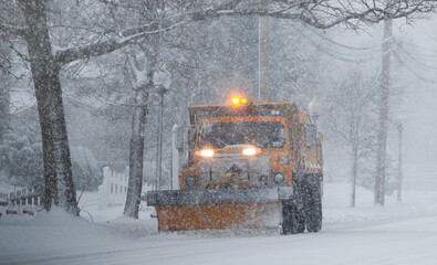 Snow falling while a yellow municipal snow plow is clearing the road