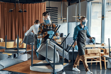 Fototapeta premium Male waiters in protective workwear arranging furniture in restaurant