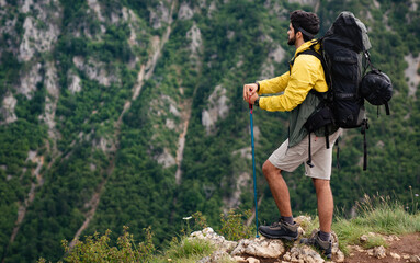 Hiker young man with backpack and trekking poles looking at the mountains in outdoor