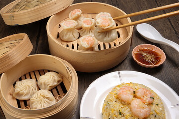 Prawn shrimp shaomai pickup by chopsticks Xiao long bao dim sum dumpling chicken prawn fish seafood vegetable in bamboo steamer fried rice on plate sauce soup spoon over rustic background