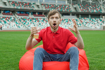 Shocked Soccer Fan in Red Tshirt With Glass of Beer Watching Football Game in Stadium Fan Zone.