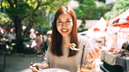 Young adult asian woman eat lunch food at restaurant outdoor on weekend day.