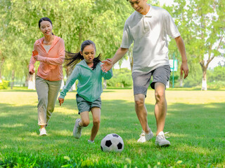 Happy family of three playing football in the park