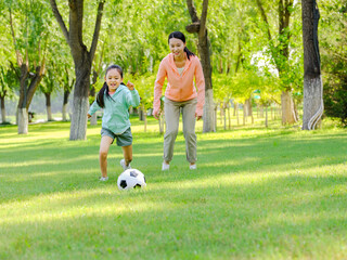 Happy mother and daughter are playing football in the park