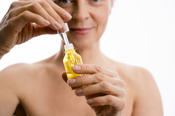 Fototapeta premium Senior lady holding bottle and receiving serum oil treatment at her face