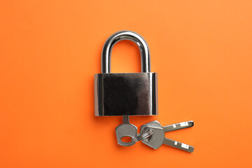 Modern padlock with keys on orange background, top view